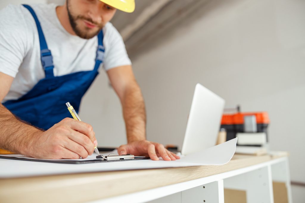 Construction worker reviewing documents with a laptop, representing streamlined AIA G702 & G703 processing using construction accounting software.